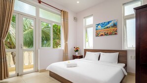 A hotel room with a large bed, a wooden headboard, a nightstand with a vase of flowers, and a painting on the wall. - Villas De Mykhe (Da Nang)