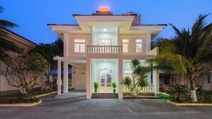 A two-story hotel with a central entrance, a balcony, and a rooftop sign. - Villas De Mykhe (Da Nang)