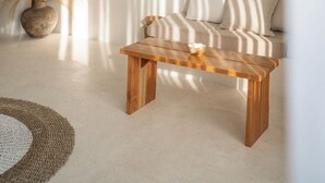 Ein schlichter Wohnraum mit einem Holztisch, einer Couch mit gestreiften Kissen und einer großen Topfpflanze.