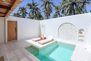 Un área de piscina moderna con dos sillones de descanso, una puerta de madera y un muro de piedra con un ventanal circular.
