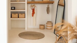Ein Zimmer mit rundbogigem Durchgang, Regalen mit Körben, einem aufgehängten Kleidungsstück, einem Spiegel und einem Korbstuhl.