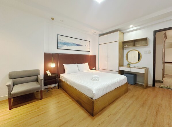A modern hotel room with a large bed, a bedside table with a lamp, a chair, a desk with a mirror, and a framed picture on the wall. - Cherysh Serviced Apartment (Ho Chi Minh City)