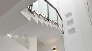 Un escalier moderne avec des rampes en verre, un détecteur d’incendie rouge et un petit luminaire fixé au mur.