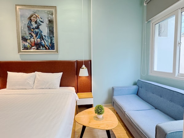 Una camera d'albergo con un letto, un divano, un tavolino con una pianta, un quadro al muro e una finestra.