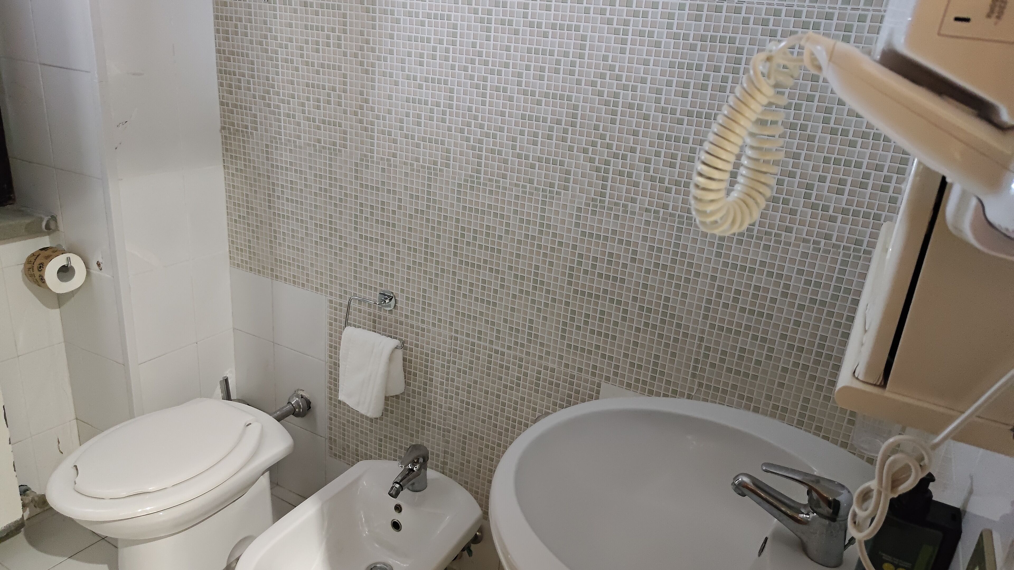 Een badkamer met toilet, bidet, wastafel en betegelde wanden.