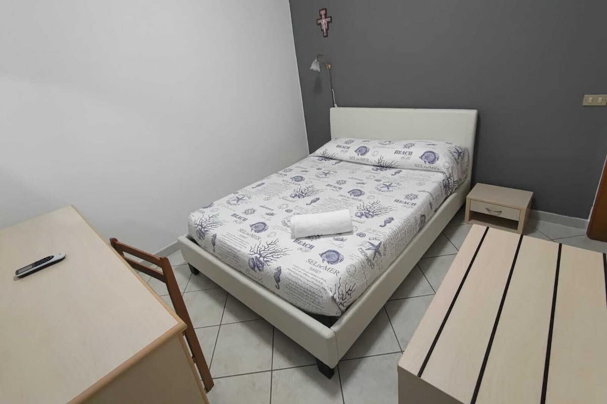 A bedroom with a bed, a desk, a chair, and a nightstand.