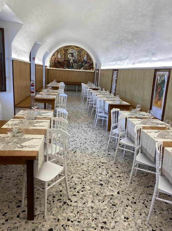 A restaurant with white chairs and tables, a terrazzo floor, and a mural on the wall. - La Locanda del Convento (Tropea)