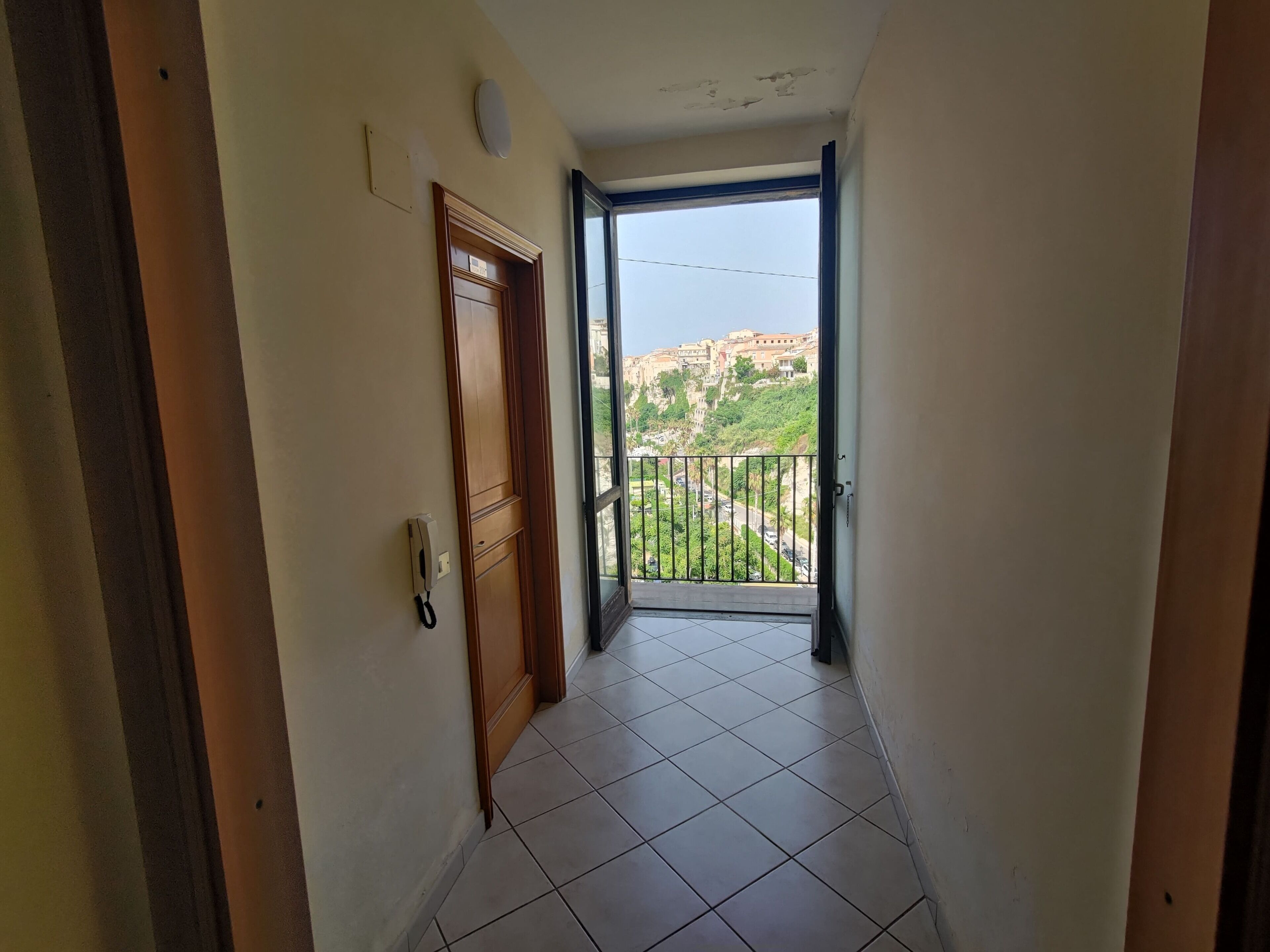A narrow hallway with a wooden door and a balcony with a metal railing.
