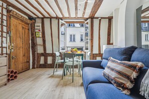 Una habitación con vigas de madera a la vista, un sofá azul, una puerta de madera y una mesa con sillas.