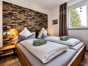 A hotel room with two beds, a stone wall, a window with a view of trees, and a bedside table.