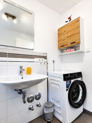 A modern bathroom with a sink, mirror, wooden cabinet, and a front-loading washing machine.