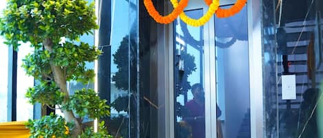 Un intérieur moderne agrémenté d’un arbre en pot, d’un ascenseur en verre et de guirlandes orange.