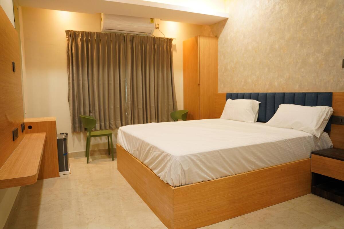 A bedroom with a wooden bed, a desk, a chair, and a window with curtains.