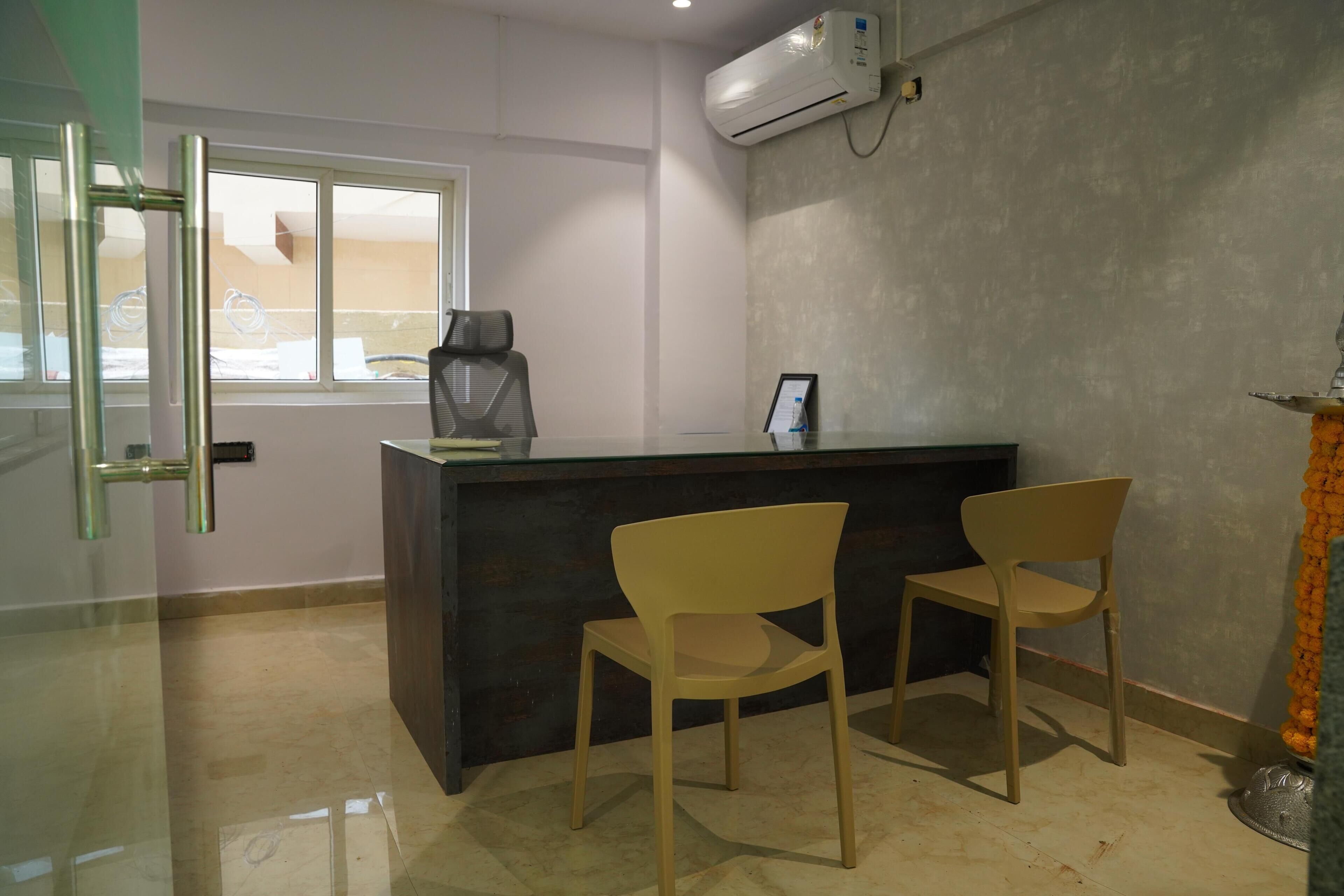 Un área de recepción con un mostrador oscuro, dos sillas de madera, una ventana con persianas y un equipo de aire acondicionado en la pared.