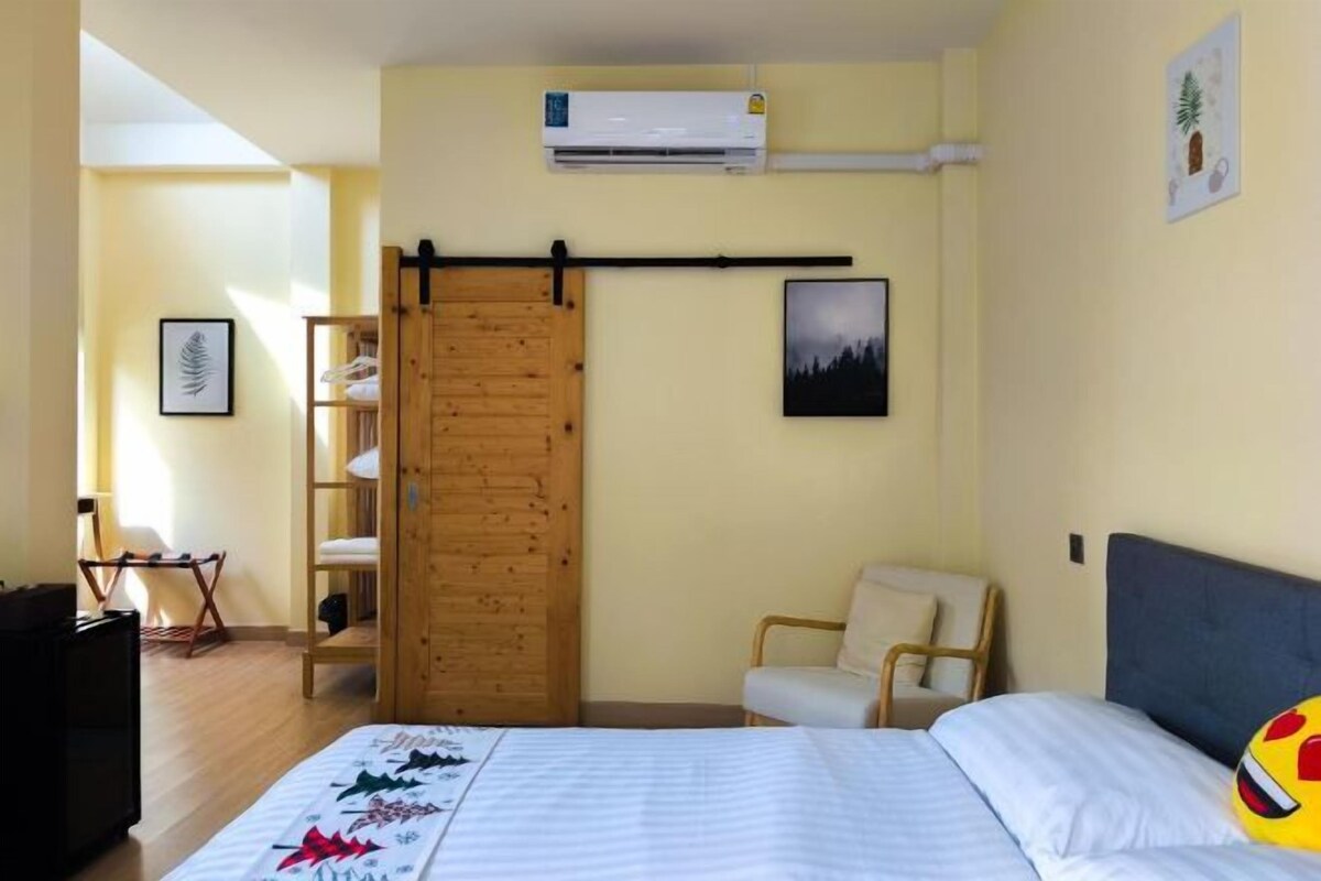 A bedroom with a bed, a wooden wardrobe, a chair, and a wall-mounted air conditioner.