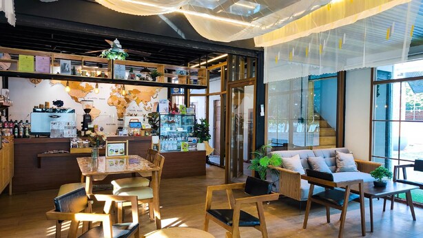 A cozy cafe with wooden furniture, a world map on the wall, and a coffee machine. - Moon in 9 haus Cafe & Villas (Rayong)