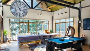 A spacious room with a pool table, a large clock, and a view of greenery through large windows. - Moon in 9 haus Cafe & Villas (Rayong)