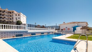 A swimming pool with a white tiled deck, a metal ladder, and a building labeled "EJF FLUIDO" in the background. - Verano Azul Seasun 90B by Casasol (Nerja)