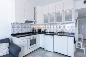 A compact kitchen with white cabinets, a black countertop, a built-in oven, and a dishwasher.