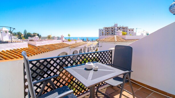 A balcony with a table and chairs, overlooking a coastal area with buildings and a clear sky. - Verano Azul Seasun 90B by Casasol (Nerja)