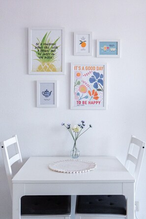 Een witte tafel met een bloemenvaas en een decoratief bord, omringd door witte stoelen.