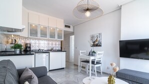 A modern kitchen with white cabinets, a dining area with white chairs, a gray sofa, and a white table with a vase. - Verano Azul Seasun 90B by Casasol (Nerja)