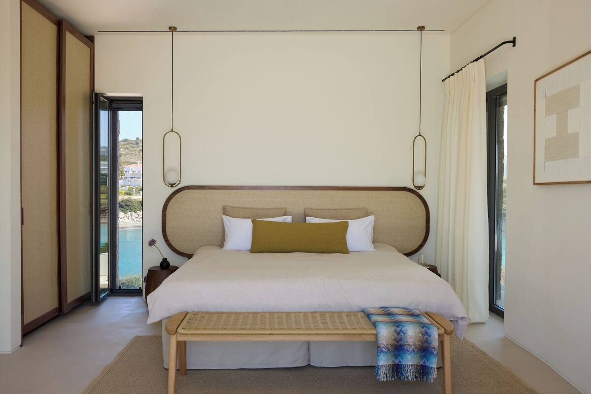 Ein Schlafzimmer mit einem großen Bett, einer Bank, einem Nachttisch und Blick ins Freie.
