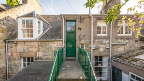 A narrow stone staircase leading to a green door, flanked by stone walls and a small window.