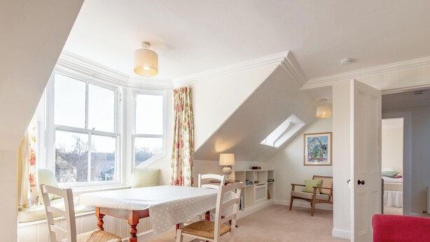 A room with a dining table, chairs, a sofa, a lamp, and a painting on the wall.