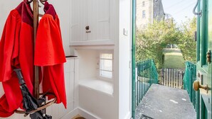 A room with a coat rack holding several red jackets, a window with a view of a green gate and a building in the background.