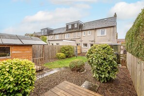 Een woonhuis met tuin, houten terras en een tweegezinshuis met veel ramen en een schuin dak.