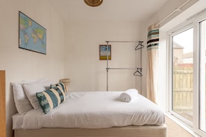 Un lit bien fait, avec du linge de lit blanc et des coussins à rayures, une carte du monde accrochée au mur et une fenêtre avec des rideaux.