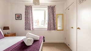 Habitación de hotel con cama, ventana con cortinas, mesita de noche con lámpara y espejo en la pared.
