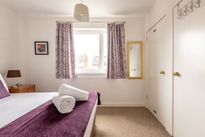 Ein Hotelzimmer mit Bett, einem Fenster mit Vorhängen, einem Nachttisch mit Lampe und einem Spiegel an der Wand.