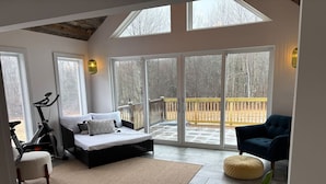 A spacious room with a large bed, a chair, a bike, and a view of a wooden deck through glass doors. - Timber Tide Retreat Just 15 Minutes to Belfast (Swanville)