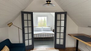 A loft bedroom with a bed, a desk, a blue sofa, and a white rug. - Timber Tide Retreat Just 15 Minutes to Belfast (Swanville)