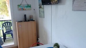 A small room with a white table, a television mounted on the wall, a wooden cabinet, and a small plant on the table. - COSY & MODERN STUDIO NEAR PORT (Agde)