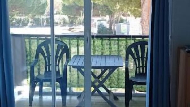 A balcony with two chairs and a table, overlooking a parking area and trees. - COSY & MODERN STUDIO NEAR PORT (Agde)