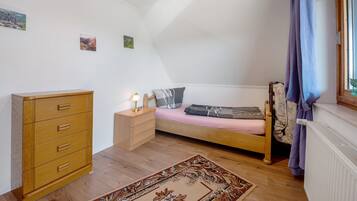 Ein Schlafzimmer mit Bett, Kommode, Nachttisch und einem Fenster mit Vorhängen.
