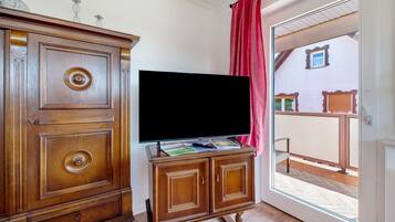 A wooden cabinet with a flat-screen TV on top, a red curtain, and a view of a balcony with a railing.