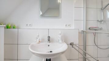 A bathroom with a white sink, two bottles of shampoo, a mirror, and a shower with a glass door.