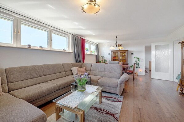 Un salon spacieux avec un canapé d’angle, une table basse en verre et un coin repas agrémenté d’un buffet en bois.
