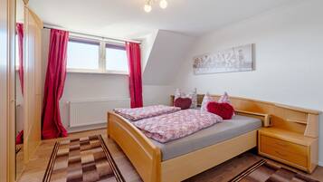A bedroom with a bed, wooden nightstand, and a window with curtains.