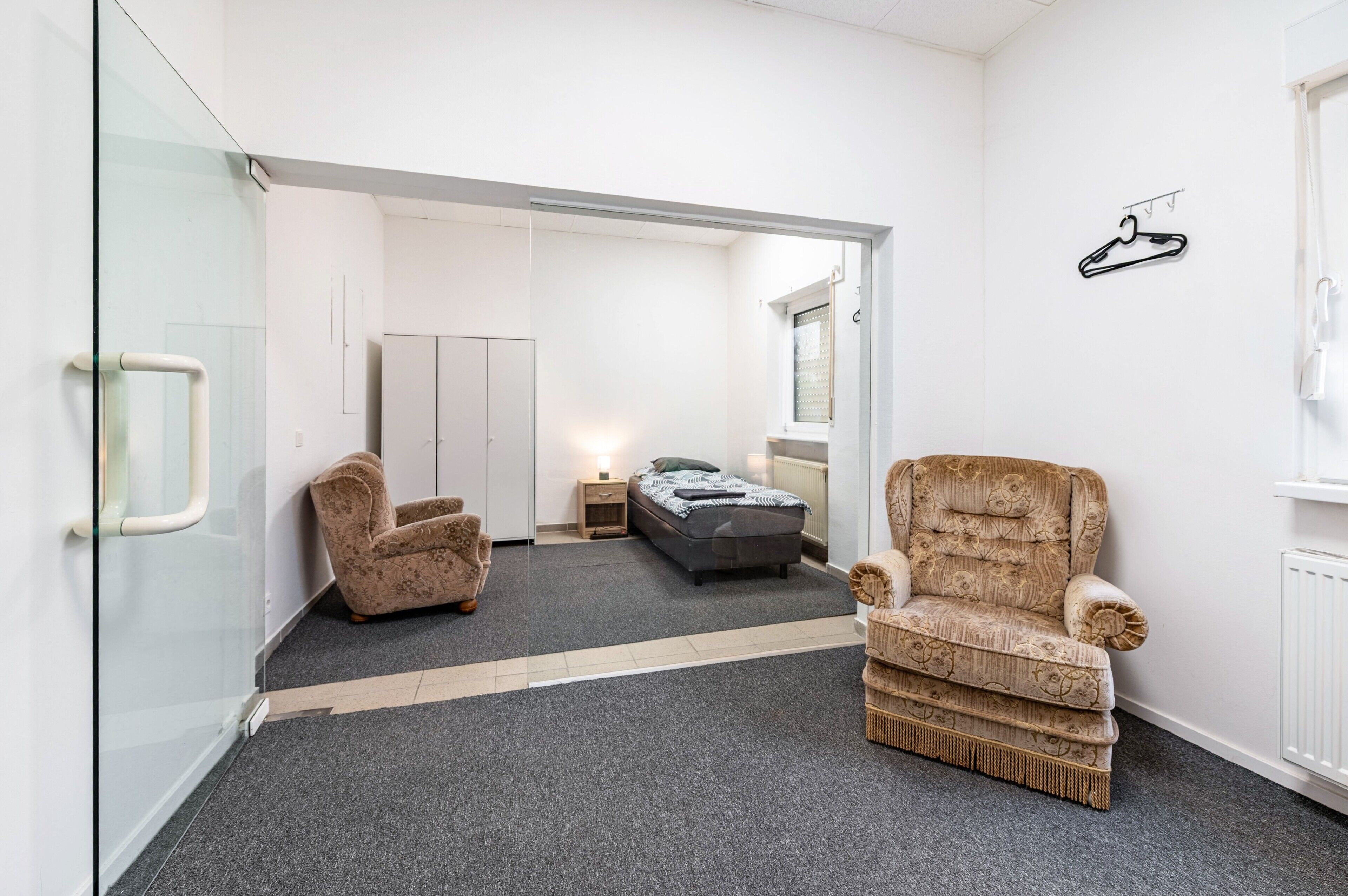Ein modernes Schlafzimmer mit Glastrennwand, einem Bett, einer Couch und einem Sessel.