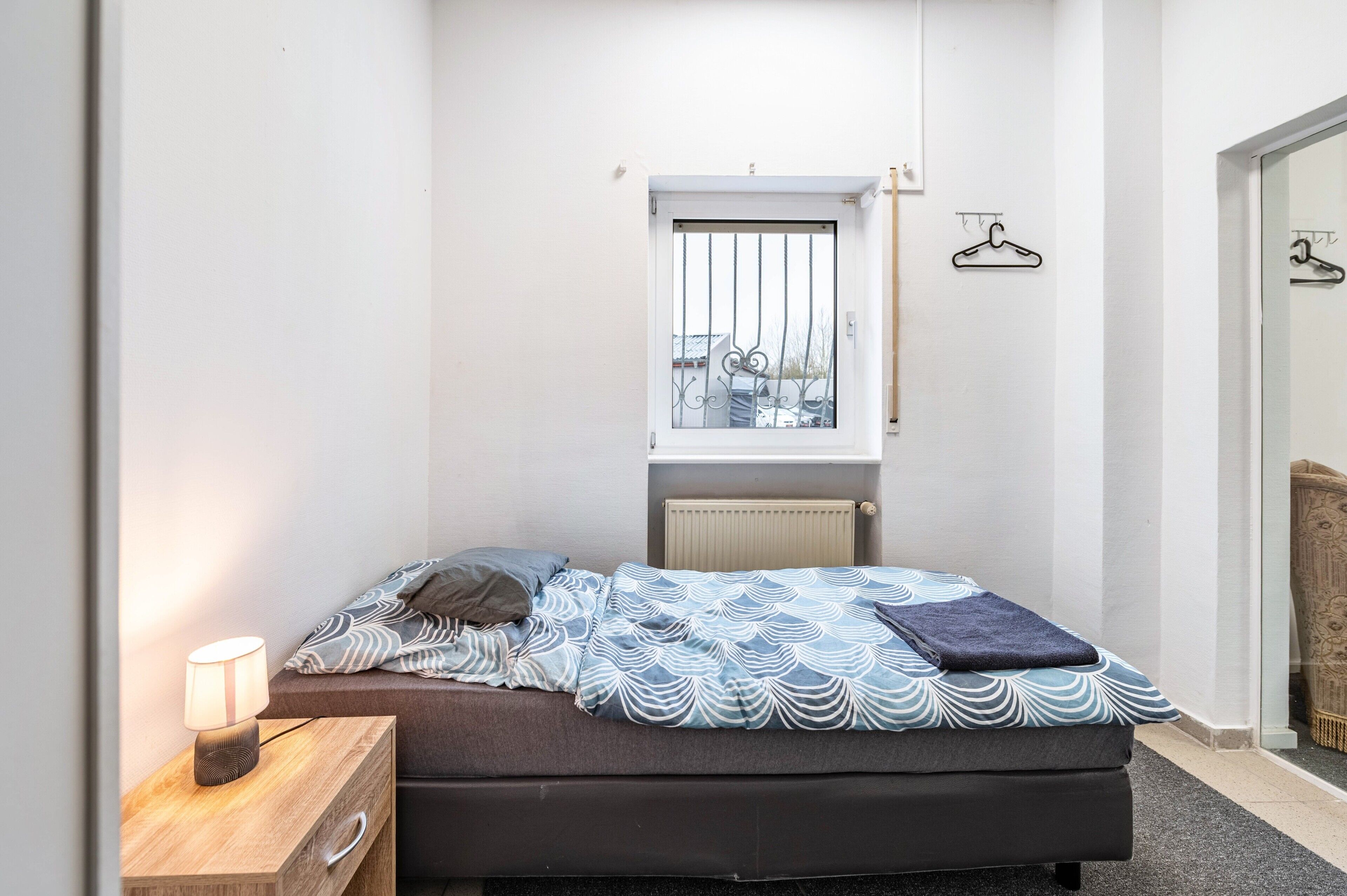 Camera da letto con un letto, comodino, lampada, finestra, termosifone e vista esterna.