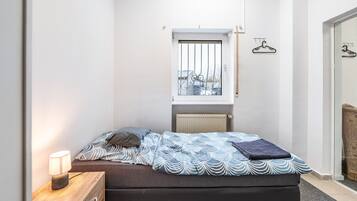 Camera da letto con un letto, comodino, lampada, finestra, termosifone e vista esterna.