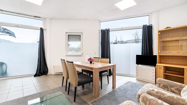 A modern living room with a dining table, chairs, a sofa, a TV, and a large window with curtains. - Holiday Apartment “SaarGlück” with Mountain Views and Wi-Fi (Beckingen)