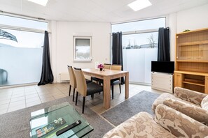 Una sala de estar moderna con una mesa de comedor, sillas, un sofá, un televisor y un ventanal con cortinas.