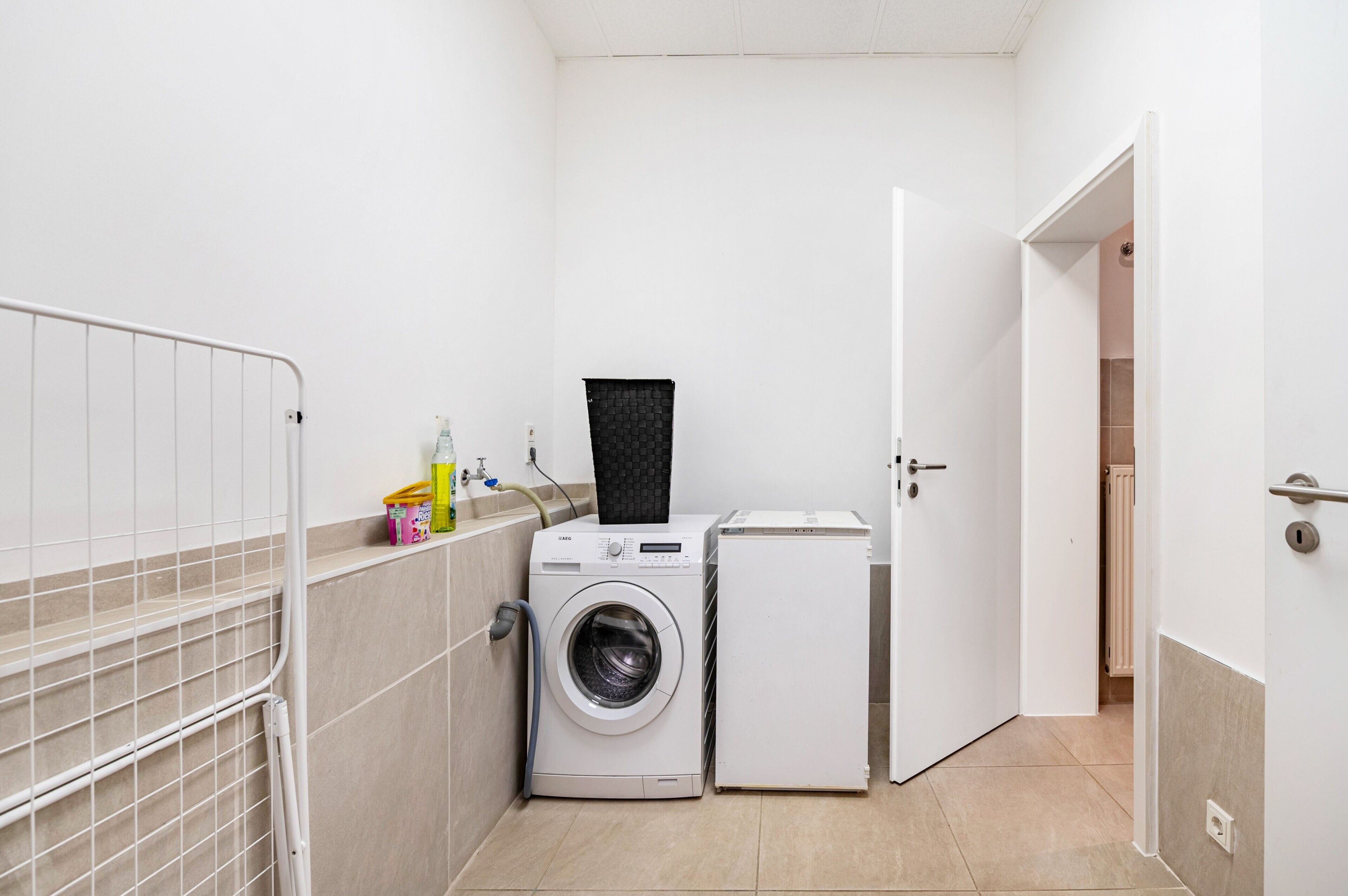 A small laundry room with a washing machine, dryer, and a metal rack.
