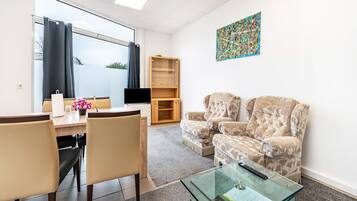 Un soggiorno moderno con un tavolino in vetro, poltrone beige, un mobile TV in legno e un'ampia finestra con tende.